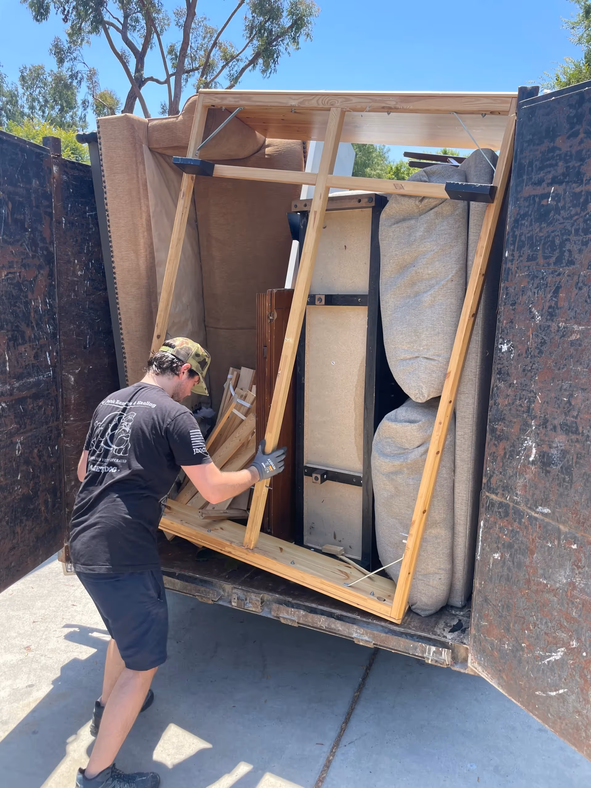 A JDog crew member loading a bed frame into a packed trailer to haul away.
